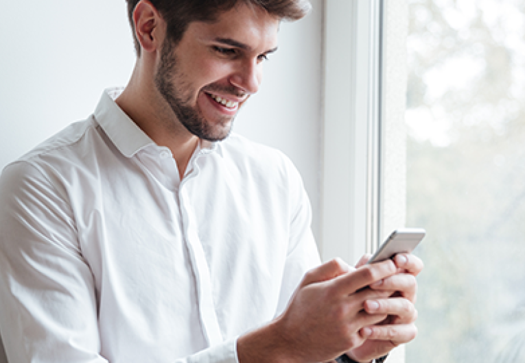 Cheerful businessman dressed in white shirt sitting and looking at phone