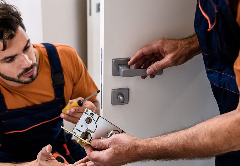 men in overalls fix lock on industrial door