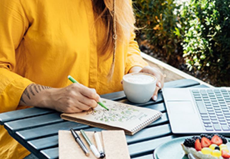 A person is coloring on a notepad while sitting at a table.
