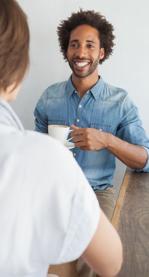 Man with a cup of coffee chatting with a person with their back to the camera